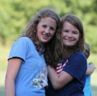 Two young female campers embracing and smiling.