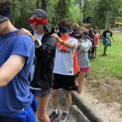 A group of blindfolded young students participating in a Camp Leadership Program team building activity.