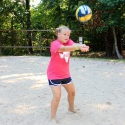 A young female camper playing volleyball on an outdoor sand court.