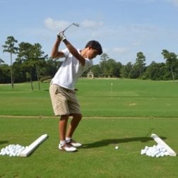 A young camper about to take a golf shot on an outdoor driving range.