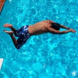 A male camper diving into the Camp Olympia swimming pool.