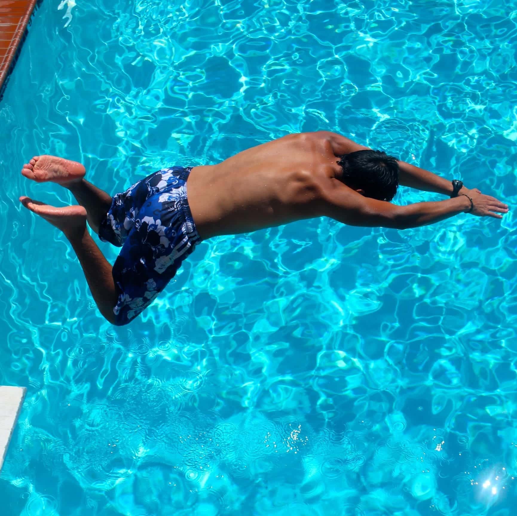 A male camper diving into the Camp Olympia swimming pool.