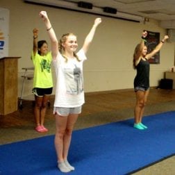 Three young female campers practicing a cheerleading routine on a practice mat.