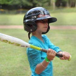 A young camper wearing a batting helmet and holding a softball bat.