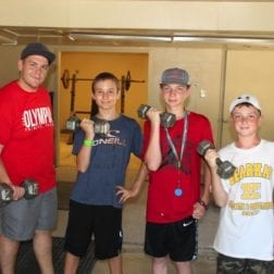 Four young male campers posing with hand weights during a workout.