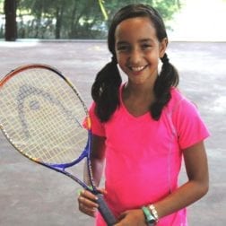 A young female camper smiling and holding a tennis racquet.