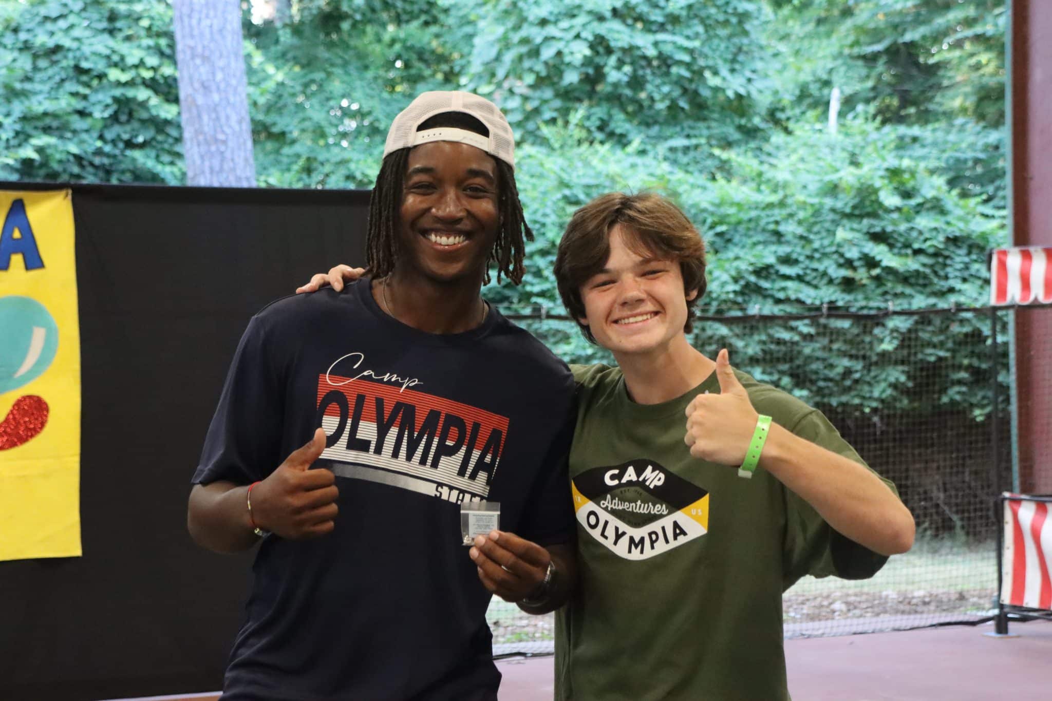 summer camp counselor in camp olympia staff shirt with boy camper thumbs up