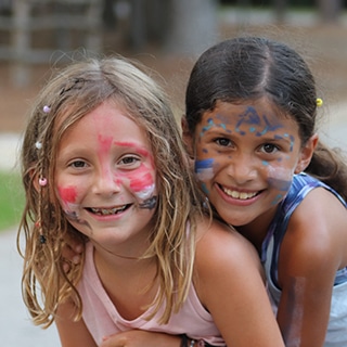 Two young girls wearing fun face paint and smiling at summer camp.