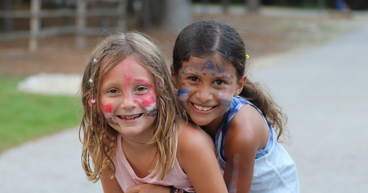Two young girls wearing fun face paint and smiling at summer camp.