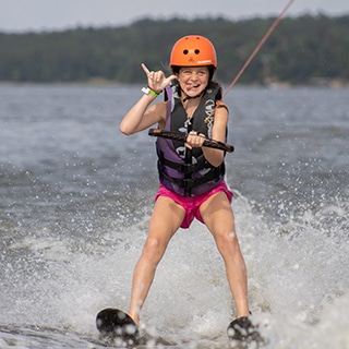 Young girl water skiing, smiling, and giving the hang loose sign.