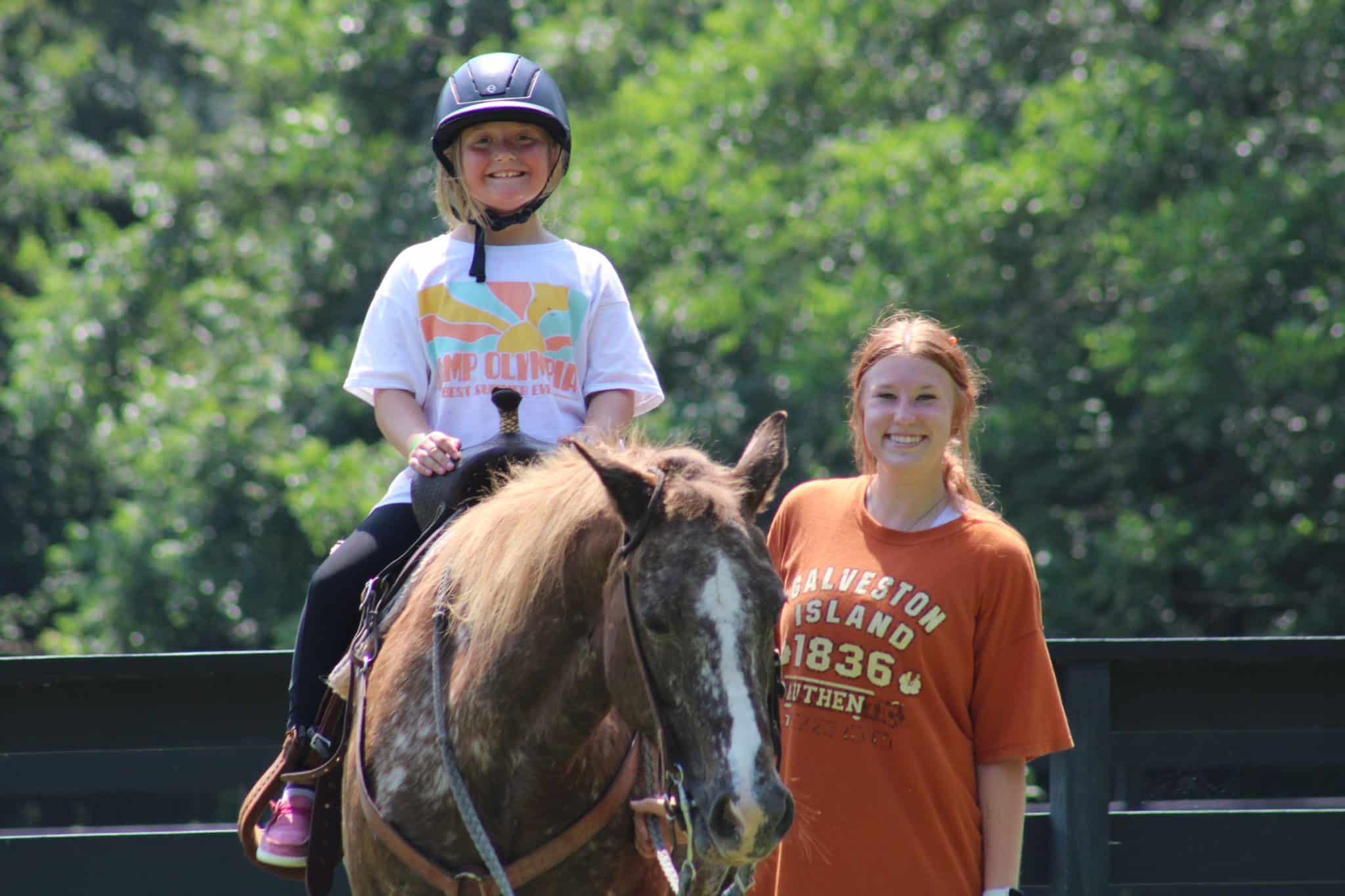 summer camp counselor helping camper on horseback