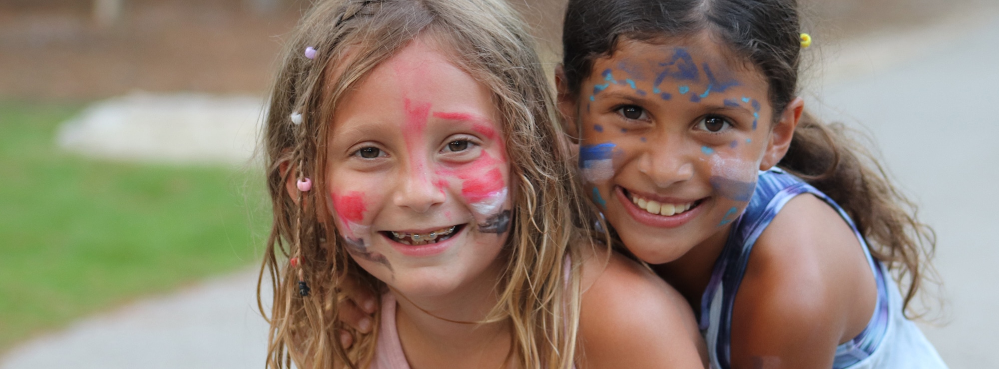 Two joyful campers with Athenian and Spartan face paint smiling at the camera.